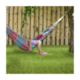 Person sitting in a colorful striped hammock on artificial grass with a wooden fence background